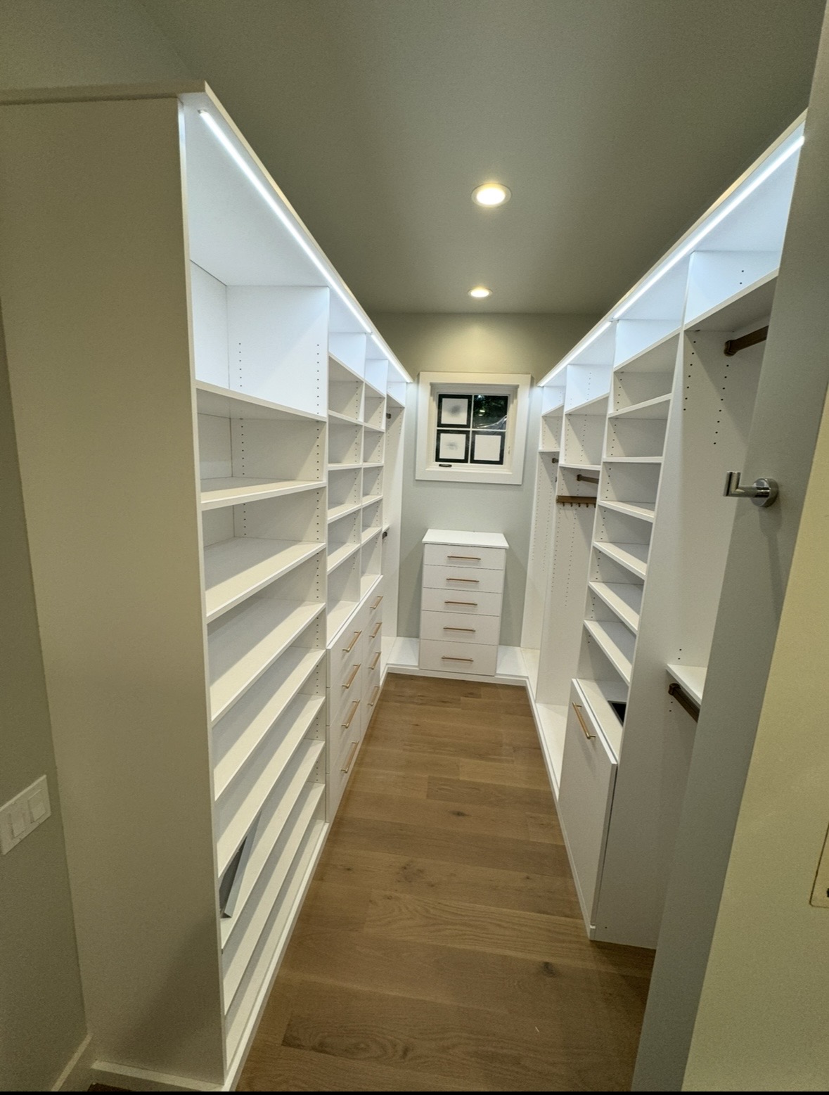 Narrow walk-in closet with full-height shelving and window