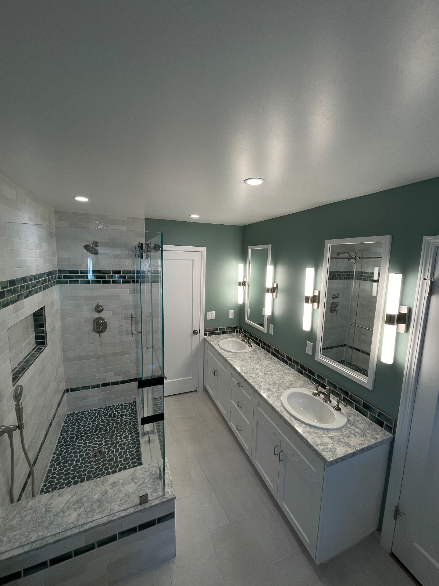 Spacious master bathroom with double vanity, marble countertops, glass shower, and sage green accent wall