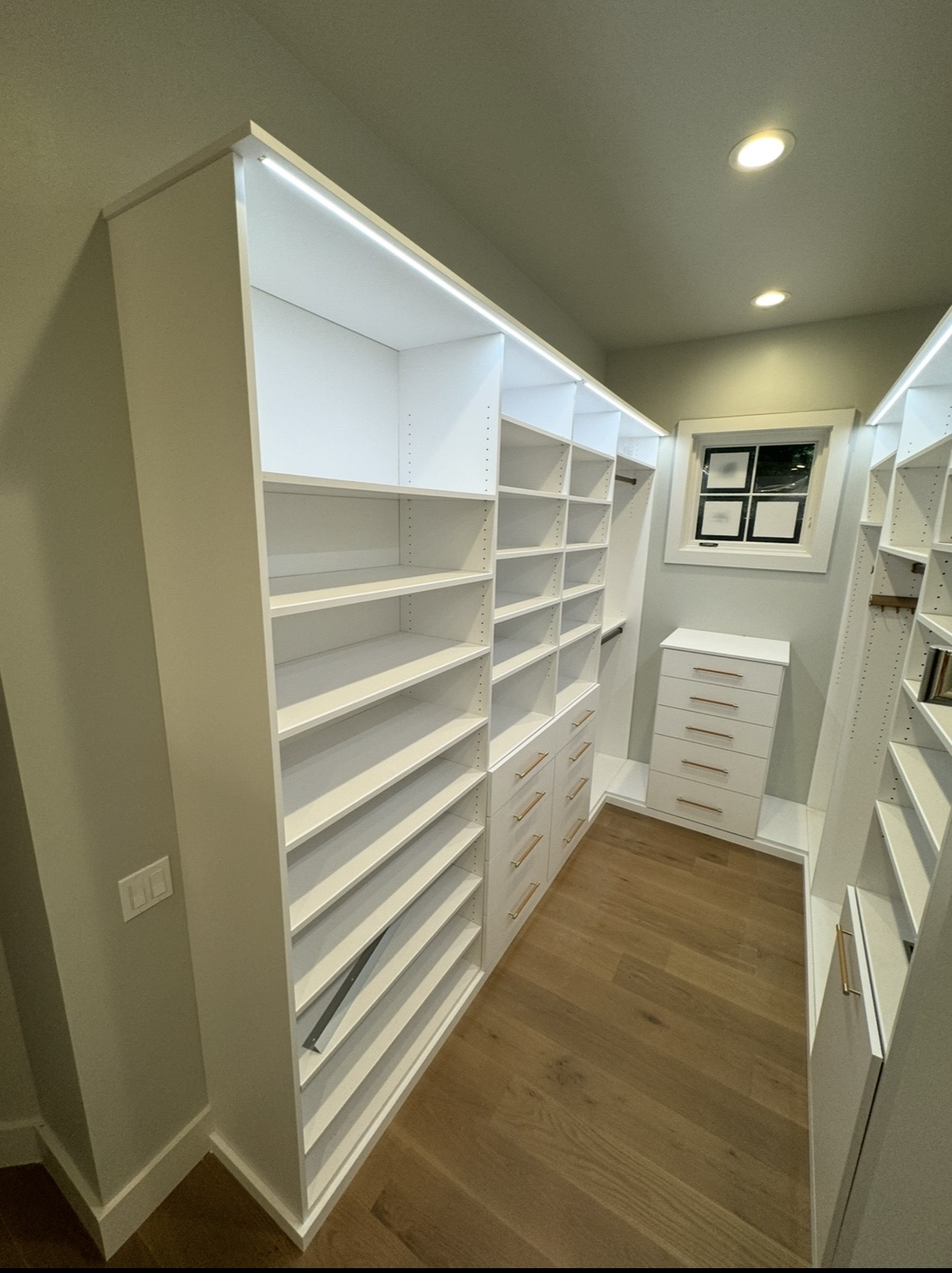 Walk-in closet with LED-lit white shelving and drawer banks